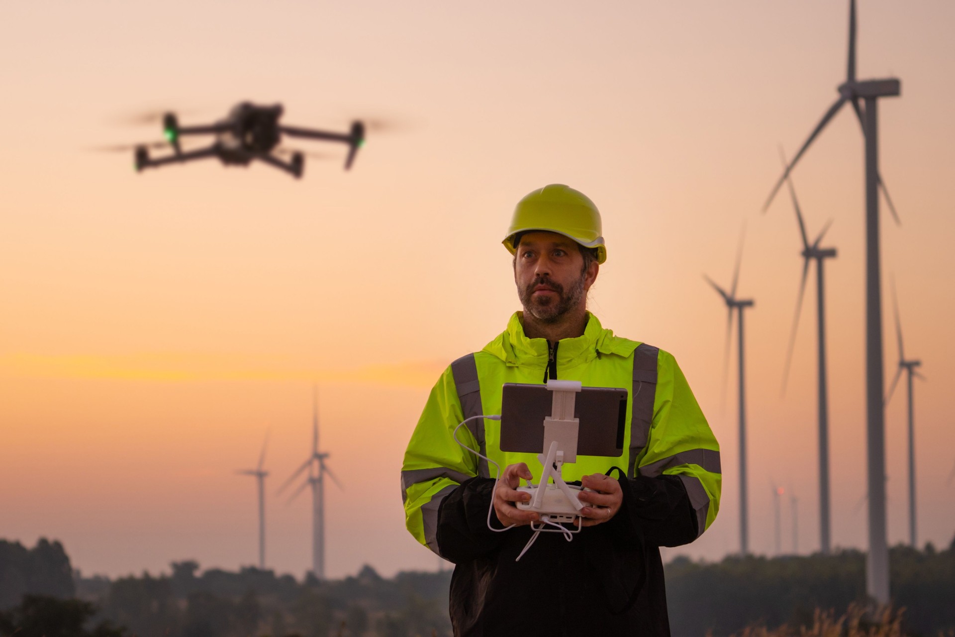 Engineers male flying drone surveying wind turbines.